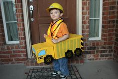 a young boy dressed up as a construction worker in front of a door with a toy truck