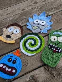 four crocheted cartoon characters are sitting on a wooden surface, each with different eyes and mouth shapes