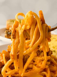 a fork full of spaghetti on top of a white plate next to another plate with meat and cheese