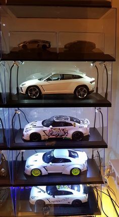 three cars are on display in a glass case with black shelves and lights behind them