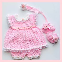 a pink crocheted baby outfit and booties on top of a white table