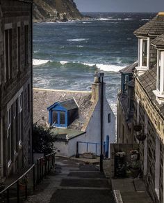 an alley way leading to the ocean with houses on either side and waves crashing into the shore