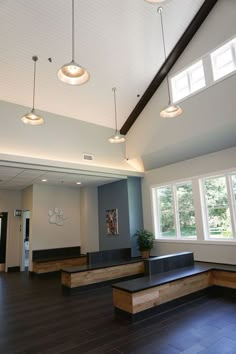 an empty room with wooden benches and lights hanging from the ceiling, along with large windows