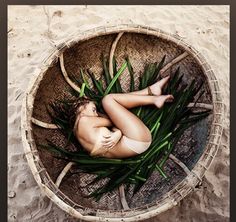 a woman laying in a basket on the beach