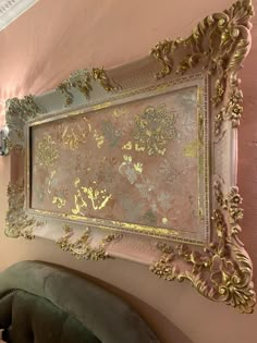 an ornate gold and silver framed artwork hangs on the wall above a green velvet chair