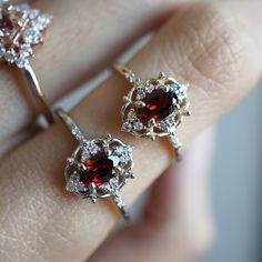 a woman's hand holding two rings with red and white stones on them,