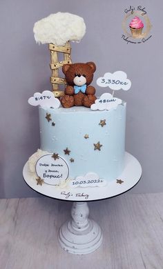 a teddy bear sitting on top of a blue cake with clouds and stars around it