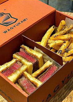 two boxes filled with sandwiches and fries on top of a wooden table