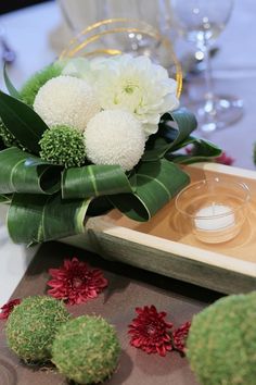 flowers and greenery are arranged on a tray at a table setting for an event