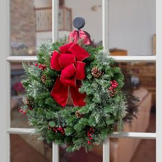 a christmas wreath hanging on a window sill with pine cones and red berries in the center