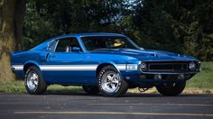 a blue muscle car parked on the side of the road in front of a tree