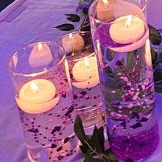 candles are lit in vases filled with water and flowers on a purple table cloth