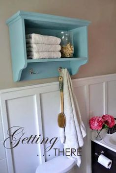 a blue shelf above a white toilet in a bathroom with pink flowers and towels on it