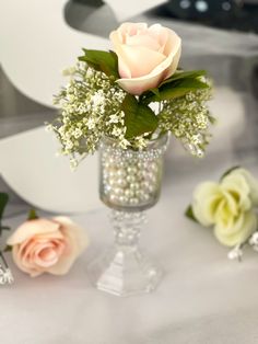 three roses are sitting in a vase on a table with other flowers and greenery