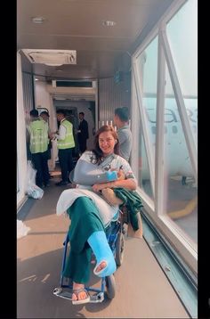 a woman sitting in a wheel chair next to an airport window with people standing around