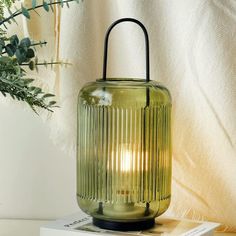 a green glass lantern sitting on top of a white box next to a potted plant