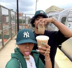 two people standing next to each other on a train platform holding drinks in their hands