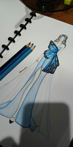 a drawing of a woman in a blue dress with pencils next to it on a table