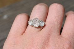 a person's hand with a three stone ring on top of their finger,