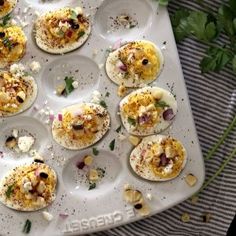 an assortment of deviled eggs on a tray with herbs and seasoning sprinkles