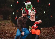 a man and woman sitting on a chair with a baby in front of a christmas tree