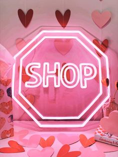 a neon sign that says shop in front of some heart shaped paper cut out hearts