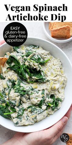 vegan spinach artichoke dip in a white bowl with crackers on the side