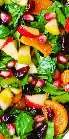 a salad with spinach, apples, oranges and cranberries in it