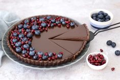 a chocolate tart topped with blueberries and raspberries next to a bowl of berries