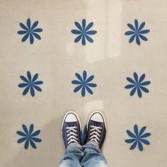 a person standing in front of blue flowers on a tile floor with their feet up