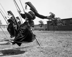 three women in graduation robes are swinging on swings