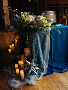 a table with candles and flowers on it next to a blue cloth covered tablecloth