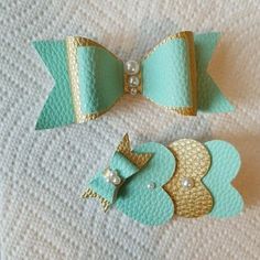 two little bows with pearls on them sitting on a white cloth covered tablecloth, one is gold and the other is mint green