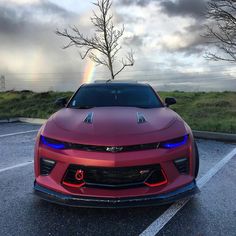 a red chevrolet camaro is parked in a parking lot with a rainbow behind it