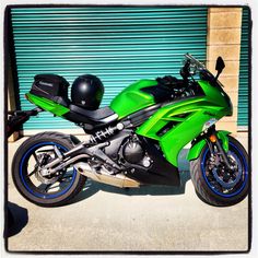 a green and black motorcycle parked in front of a garage door with roller shutters