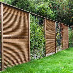 a row of wooden fences with plants growing on the fence and in between them are green grass