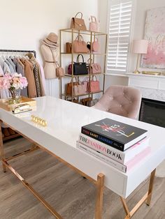 a white table topped with lots of books next to a pink chair and shelf filled with purses