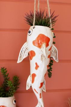 a ceramic fish hanging from a rope next to potted plants