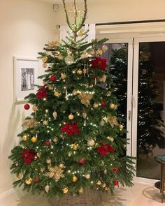 a decorated christmas tree with red and gold ornaments in a basket on the floor next to an open door