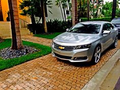 two silver cars parked on the side of a road next to palm trees and bushes