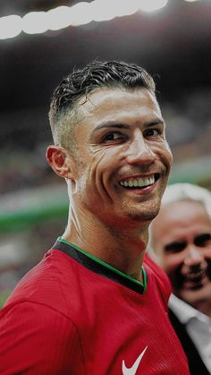 a man in a red shirt smiles at the camera while standing next to another man