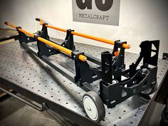 a metal work bench with wheels and orange bars on the back end, in front of a sign that reads go meatcraft