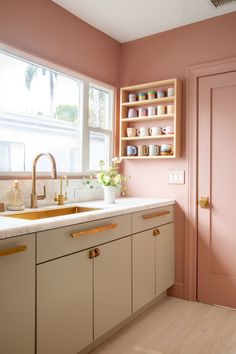 a kitchen with pink walls and white counter tops next to a wooden cabinet in front of a window