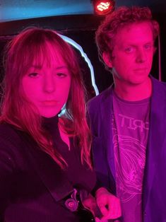 a man and woman standing next to each other in front of a neon colored background