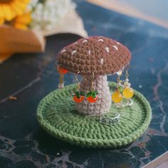 a small crocheted mushroom on top of a green plate with earrings hanging from it