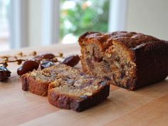 a sliced loaf of banana bread sitting on top of a wooden cutting board next to raisins