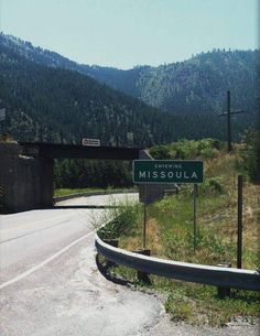 a highway sign on the side of a road in front of some hills and trees