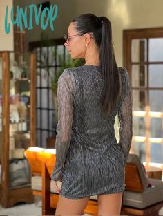 a woman with long hair and glasses standing in front of a window wearing a dress