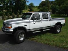 a white truck parked on the side of a road next to a lush green field