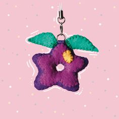 a purple flower with green leaves hanging from a metal hook on a pink background,